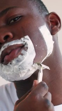 Dikey video. Tıraş rutini. Yüz bakımı. Kozmetik ürünü. Keskin usturayla beyaz nemlendirici köpük losyonlu kendine güvenen adama yaklaş..