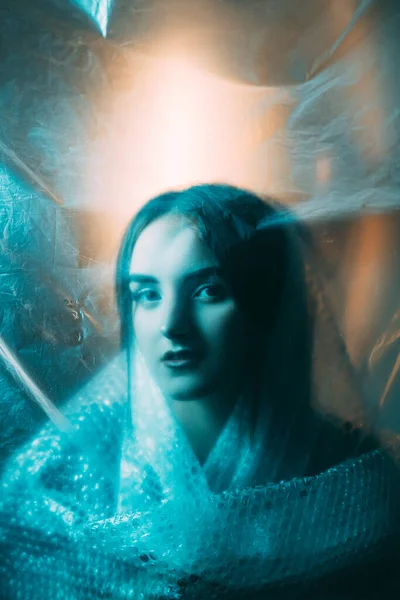 Saint face. Art portrait. Sacred beauty. Blue color light defocused pretty woman silhouette in bubble wrap behind distressed wrinkled polyethylene plastic film.