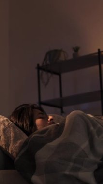 Dikey video. Uyku bozukluğu. Gece endişesi. Stres uykusuzluğu. Huzursuz, yorgun bir adam karanlık bir evde rahatsız bir kanepede uyanıyor..
