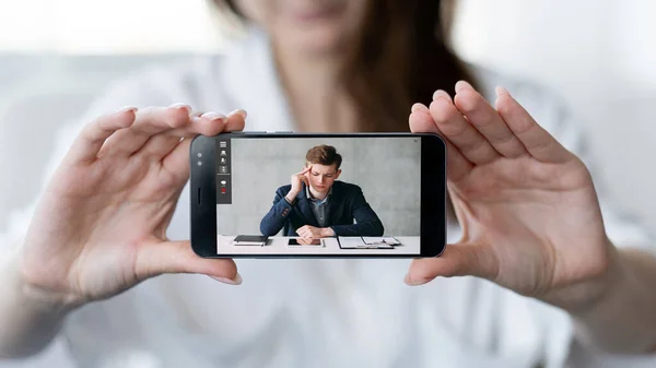 Mobile conference. Video call. Virtual meeting. Woman showing pensive tired business man on phone screen at digital office workplace.