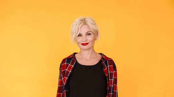 Feminine power. Beautiful woman. Stylish smiling middle-aged blonde lady red lipstick casual look posing yellow.
