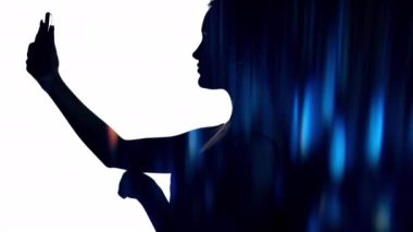 Dijital romantizm. Selfie öpücüğü. İletişim teknolojisi. Çift pozlu bulanık neon parlaklığı. Profil kadın siluetinde beyaz, siyah, boş alanda telefonla el sallayan parlak ışık..