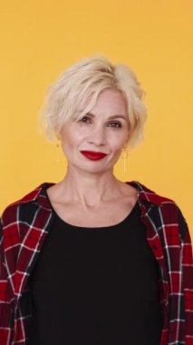 Dikey video. Kadınsı güç. Güzel kadın. Şık, orta yaşlı, sarışın kadın kırmızı ruj. Sarı poz veriyor..