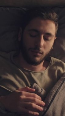 Dikey video. Kabus stresi. Uyku sorunu. Huzursuz bir gece. Kötü bir rüyadan uyanan korkmuş bir adam karanlık bir yatak odasında..