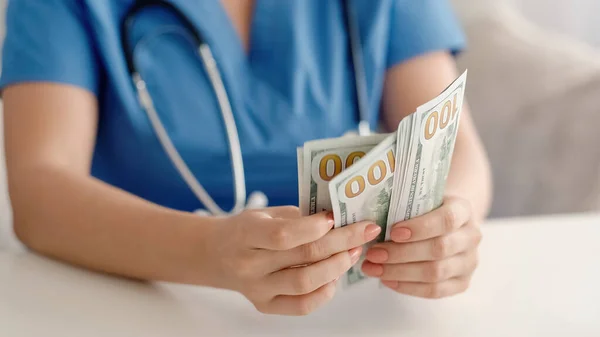 Doctor money. Healthcare cost. Medic income. Closeup of unrecognizable female physician hands counting 100 bill American US dollar banknotes cash.