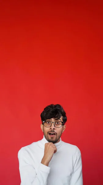 Impressed face. Surprising news. WOW reaction. Inspired amazed curious smart man in glasses with open mouth on red color empty space advertising background.