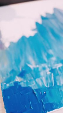 Dikey video. Boyama işlemi. Kadın ressam. Sanatsal aletler. Tanımlanamayan kadın spatulayı temizlerken beyaz tuvalde soyut bir resim oluşturuyor..