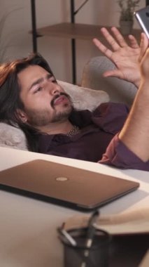 Dikey görüntülü sohbet. Sanal toplantı. İnternet iletişimi. Rahat iş adamı evde koltukta uzanmış telefonla iş hakkında konuşuyor..