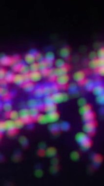 Dikey video. Bokeh ışığı. Neon parıltısı. Dijital işaret fişeği. Odaklanmamış floresan mor mavi yeşil renk koyu siyah soyut arka planda parıldıyor..