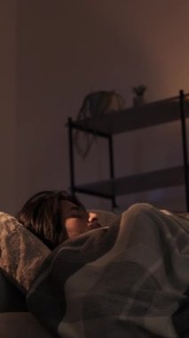 Dikey video. Uyku bozukluğu. Gece endişesi. Stres uykusuzluğu. Huzursuz, yorgun bir adam karanlık bir evde rahatsız bir kanepede uyanıyor..