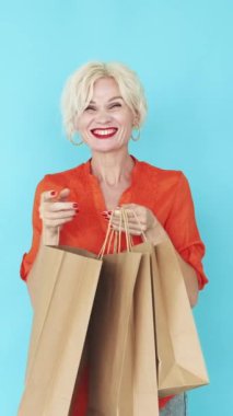 Dikey video. Tatil alışverişi. Mutlu kadın. Şenlik indirimi. Heyecanlı bir kadın mavi poz veren kağıt torbalara bakıyor..