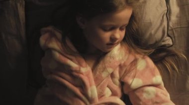 Dikey video. Çocuk yatma vakti. İyi geceler. Ebeveyn bakımı. Anne battaniyeyle örtülmüş, sakin, küçük bir kız geceleri karanlık bir yatak odasında uyuyor..