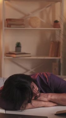 Dikey video. Masa uykusu. Öğrenci yorgunluğu. Yorucu bir eğitim uykusu. Ev içi kitaplarla iş yerinde uyuyan yorgun tembel adam..