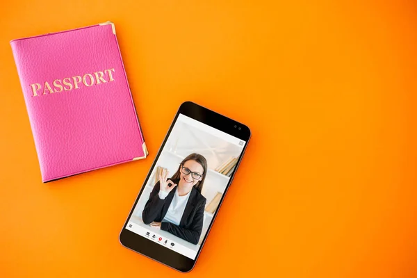 Passport service. Online expert. Digital immigration center. Satisfied business woman approving visa with okay gesture on phone screen on orange copy space background.