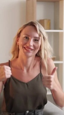 Dikey video. Birçok beğeni. Hareketli kadın. Neşeyi onaylıyorum. Mutlu bayan baş parmağını kaldırmış dans ediyor. Koltuğun içinde kendini iyi hissediyor..