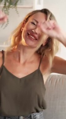 Dikey video. Mutlu heyecanlar. Neşeli kadın. Kazanan neşe. Neşeli bayan dans ediyor, el ele, oturma odasının iç tarafında koltukta oturuyor..