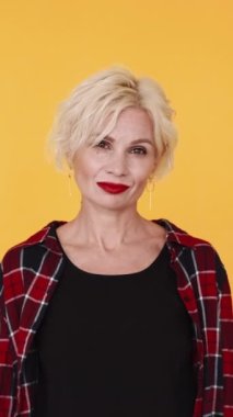 Dikey video. Kadınsı güç. Güzel kadın. Şık, orta yaşlı, sarışın kadın kırmızı ruj. Sarı poz veriyor..