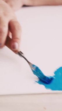 Dikey video. Soyut resim. Boyama işlemi. Yaratıcı stüdyo. Tuvale spatula ve mavi boyalarla resim çizen tanınmayan bir kadın..