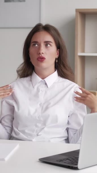 垂直录像 炎热的一天 工作的女人酷热难忍穿着白衬衫的优雅女士坐在写字台上 开着笔记本电脑 双手在屋里吹风 — 图库视频影像