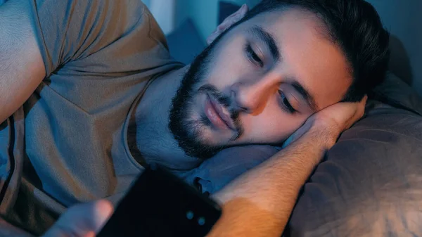 ガジェットの夜 遅いオンライン ソーシャルメディアレジャー 退屈眠い疲れ落ち着きのない男使用して電話ブラウジングインターネットでベッドで暗い寝室 — ストック写真