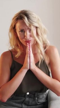 Dikey video. İçtenlikle rica ediyorum. Dilenci kadın. Umut dolu duygular. Dua eden bir kadının el ele tutuşması. Kanepenin iç tarafında oturup iyilik istemesi..