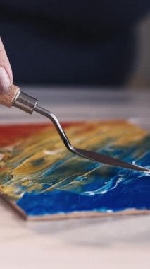 Dikey video. Resim okulunda. Sanat eseri yaratımı. Kadın ressam. Tanımlanamayan bir kadın, renkli spatula resimleriyle tuvalde soyut bir resim oluşturuyor..