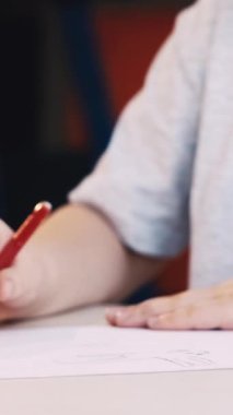 Dikey video. Aşkı resmetmek. Sanatçı çocuk. Hobi olarak. Beyaz kağıt üzerine kalem çizen tanınmamış bir kız masasının iç tarafında oturuyor..