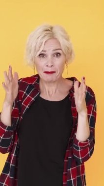 Dikey video. Öfkeli bir kavga. Münakaşa eden kadın. Öfke ifadesi. Yüzünü buruşturan orta yaşlı bağıran kadın ellerini kaldırıp sarıya poz veriyor..