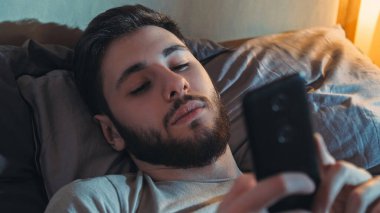 Yatak telefonu. İnternet gecesi. Gadget yorgunluğu. Sıkıcı yorgun adam karanlık yatak odasında cep telefonu okuyarak mesaj kaydırıyor..