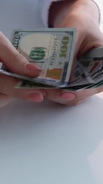 Dikey video. Nakit para. Banka hesabı. Finansal depozito. İş kadınlarının eli beyaz arka plandaki 100 dolarlık banknotları kredi kartıyla sayıyor..