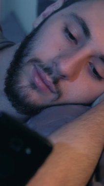 Dikey video. Gadget gecesi. İnternette geç kaldım. Sosyal medya eğlencesi. Sıkılmış, uykulu, yorgun, huzursuz adam. Karanlık yatak odasında internette geziniyor..