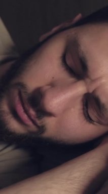 Dikey video. Kabus korkusu. Uyku sorunu. Gece uykusuzluğu sorunu. Endişeli, korkmuş bir adam, karanlık bir yatak odasında, kabustan uyanır..