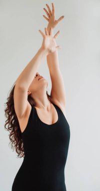 Zarif dans. Kadınsı zarafet. Rahatlamış kadın kollarını kaldırarak müzik yapıyor. Beyaz arka planda izole edilmiş sakin ve keyifli atmosferin tadını çıkarıyor..