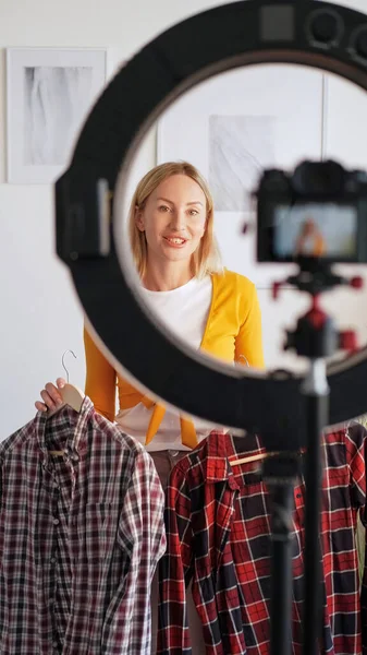ファッションブログの撮影 スタイリストコンテンツ 三脚リングライト上のカメラを使用してシャツ新しいコレクションを示す友好的な女性のビデオVogueブログを記録してください — ストック写真