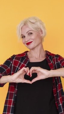 Dikey video. Aşk bakımı. Etkilenmiş kadın. Duyguların ifadesi. Orta yaşlı mutlu bir bayan el ele tutuşup sarıya kalp şeklinde bir jest yapıyor..