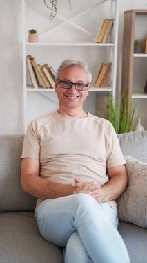 Mutlu adam. Dinlenmenin tadını çıkarıyorum. Ev tatili. Gülümseyen yaşlı erkek, hafif bir evde koltukta oturuyor..