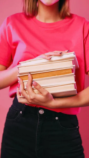 Literature exam preparation. Educating reading. Unrecognizable girl holding stack of books isolated on neon color pink background.