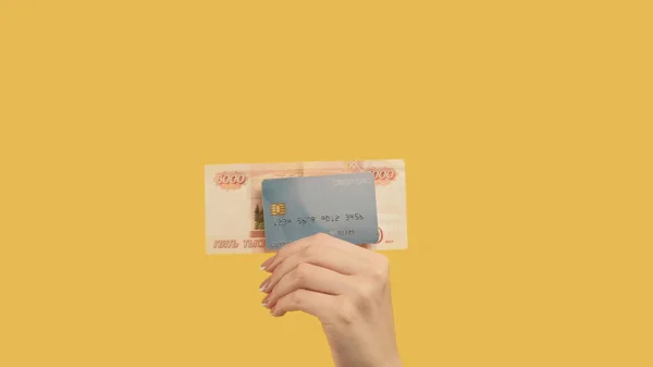 Money loan. Bank transaction. Woman hand holding rubles 5000 and credit card on yellow background.