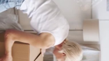 Dikey video. Eve gidiyoruz. Mutlu taşınmalar. Yeni bir hayat. Neşeli son sınıf kadını dans ediyor. Hafif apartmandaki kutulardan eşyaları boşaltıyor..