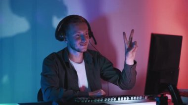 Gece eğlencesi. Barış jesti. Gülümseyen adam kusursuz döngü gösteriyor. Takipçilerle iletişim kuruyor. Siber takım arkadaşları karanlık neon ışıklı odayı selamlıyor..