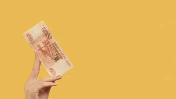 Bank deposit. Mortgage payment. Female hand holding rubles showing 5000 cash on yellow background copy space.