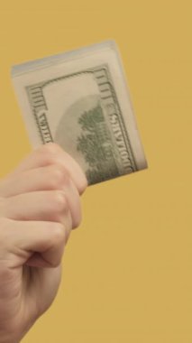Dikey video. Yatırım geliri. Finansal başarı. Kadın eli, sarı arka planda 2 dolar teklif ediyor..