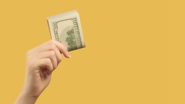 Investment income. Money loan. Female hand gesture holding dollars on yellow background copy space.