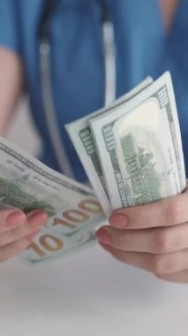 Dikey video. Doktor parası. Sağlık sigortası masrafı. Sağlık geliri. Tanımlanamayan kadın doktorların 100 'lük banknotları sayması nakit..