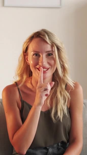 垂直ビデオ 秘密を守るんだ 静かな女性 顔の表情 笑顔女性でカジュアルルック保持シャープな指で口の中に光の部屋のインテリア — ストック動画