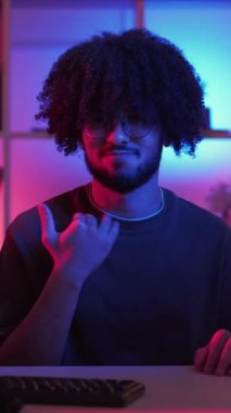 Dikey video. Bu kadar hareket. Reddeden adam. Meme ifadesi. Protestocu adam, koyu neon ışıklı odada el sallayarak masa başında oturuyor..