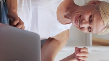 Dikey video. Çevrimiçi sohbet. Mesafe iletişimi. Sosyal ağ. Rahatlamış, olgun bir kadın evdeki koltukta dizüstü bilgisayar kullanarak mesaj okuyor..