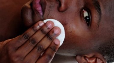 Dikey video. Yüz temizleme. Cilt bakımı. Hijyen nemlendirici. Kendine güvenen bir adamın yüzüne toner sürerek pamuk bloknotları yürüttüğü yakın plan..