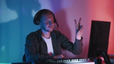 Gece eğlencesi. Barış jesti. Gülümseyen adam kusursuz döngü gösteriyor. Takipçilerle iletişim kuruyor. Siber takım arkadaşları karanlık neon ışıklı odayı selamlıyor..