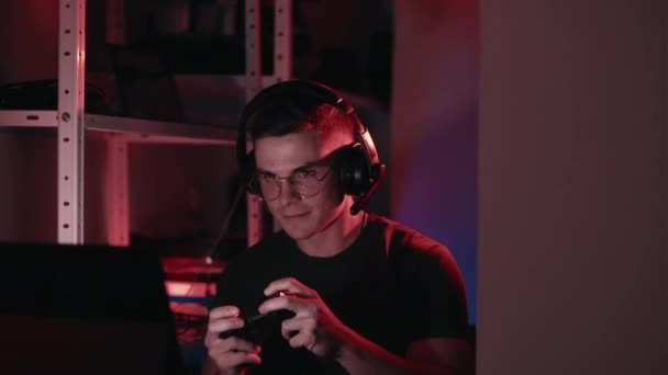 ビデオゲーム オンライントーナメントで優勝 興奮した男でヘッドフォンや眼鏡を使用してコンピュータを再生コンソール喜びで自宅で暗い光の部屋に座って — ストック動画